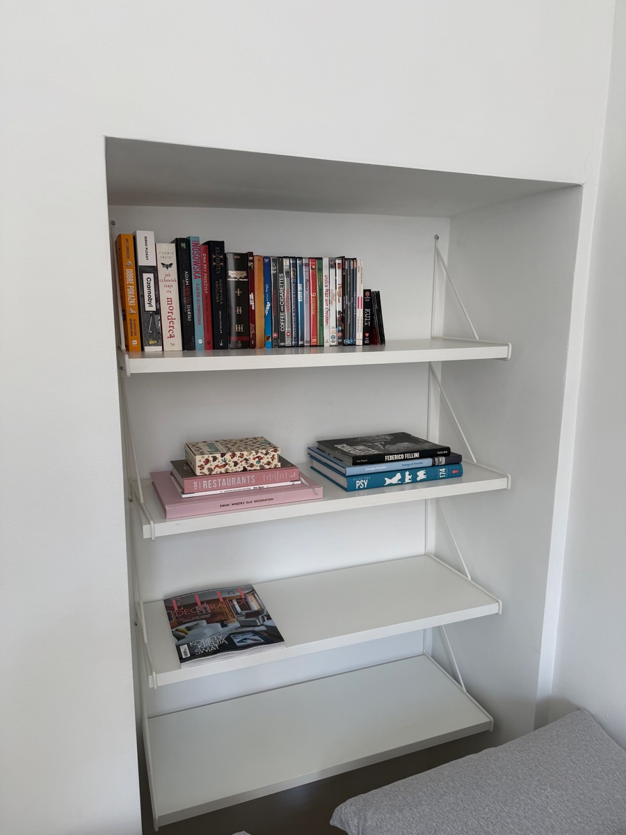 Built-in alcove shelving with books, films and design magazines beside the bed