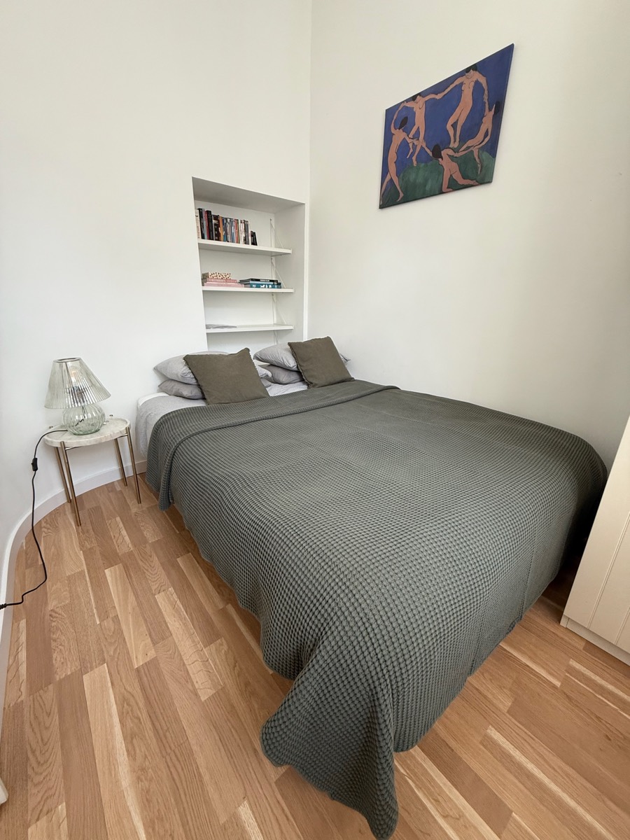Double bed under a sage waffle bedspread, with alcove bookshelves and a Matisse dancers print