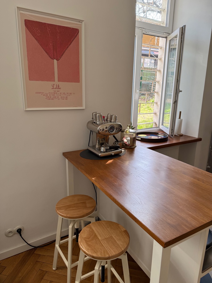 Oak breakfast bar with two stools and a chrome espresso machine beside a window open onto the courtyard