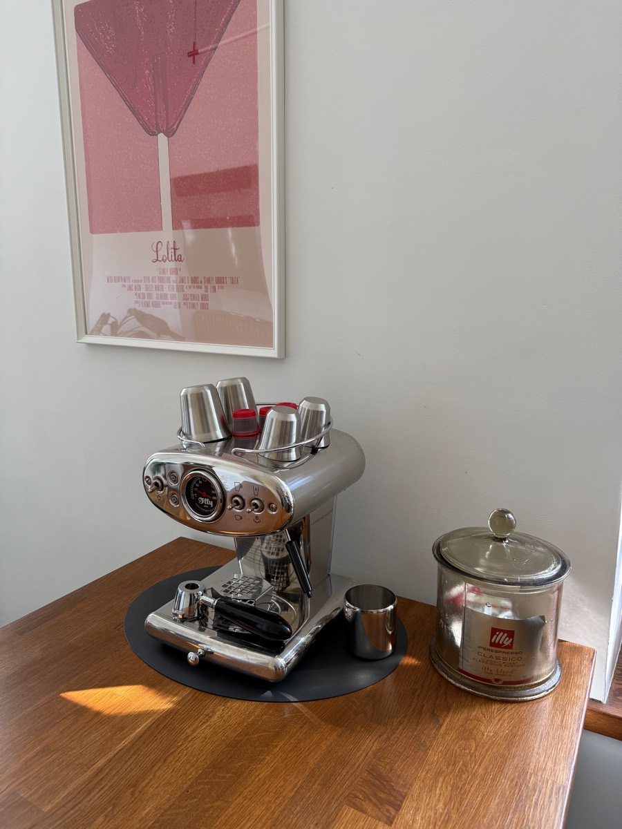 Chrome espresso machine and coffee canister on the oak bar under a framed film poster