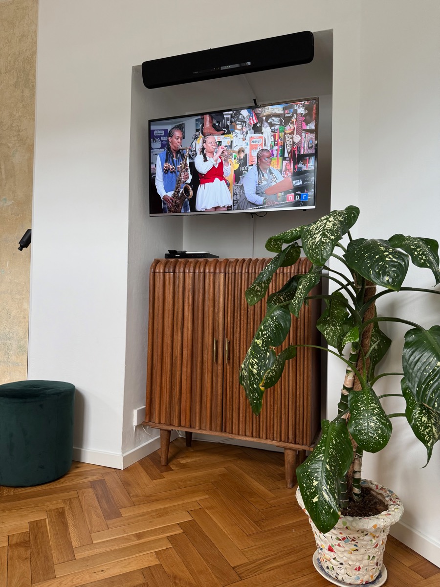 Television playing in the plastered niche above a fluted walnut cabinet, green velvet pouf alongside